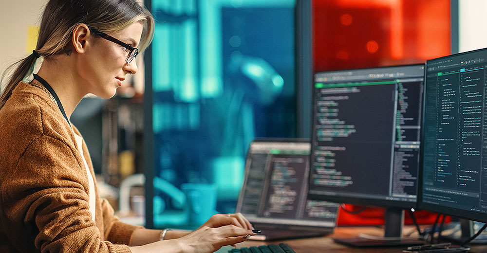 A SaaS platform developer working on dual monitors in an innovative office setting